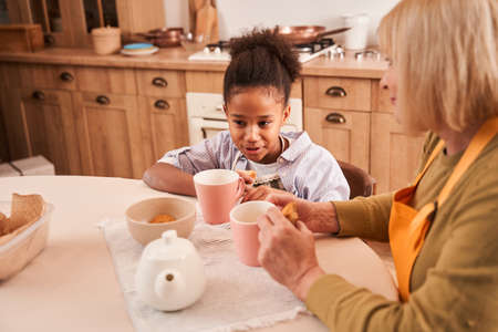 Emotional daughter teenager chatting with her happy mom while enjoying cookiesの写真素材