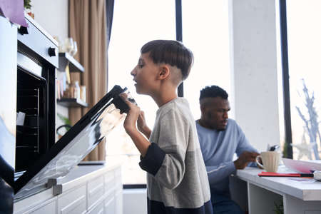 Curious caucasian boy looking into the oven while waiting for the breakfastの写真素材