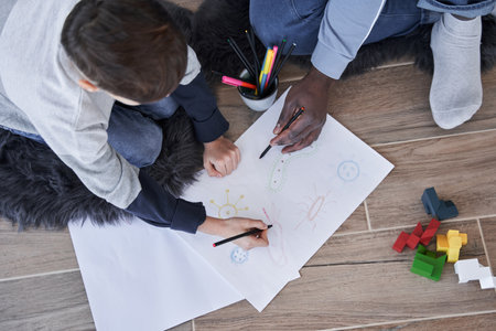 Multiracial father telling something to his son while he is drawing at the floor attentively