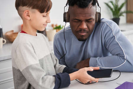 Multiracial man looking at the smartphone screen with serious face while choosing songsの写真素材