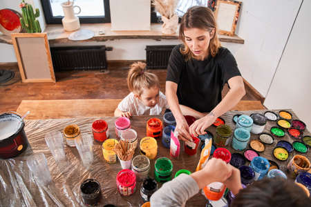 Little girl looking at the paints while her mother opening it at the tableの写真素材