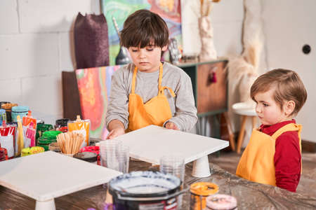 Little brother boys standing at the table and preparing to the drawing at the art class