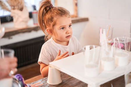 Female child looking at somebody attentively while standing at the table with paintsの写真素材
