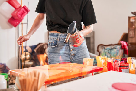 Woman holding gas-burner and using it into the painting while drawing at the fluid art techniqueの写真素材