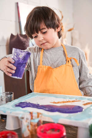 Child holding paints at the glass and painting on the canvas while spending time at the art schoolの写真素材