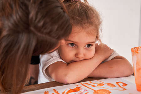 Sad caucasian female child sitting at the table while her lovely teacher calming her