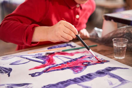 Caucasian child drawing fish at the paper with brush and acrylic paintsの写真素材