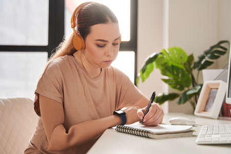 Caucasian girl with artificial limb writing at the notebook while preparing her homework