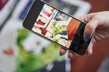 Female graphic designer holding smartphone and shooting her art works