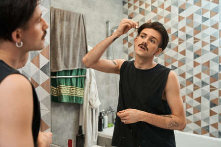 Joyful handsome guy holding glass dropper and bottle of liquidの写真素材
