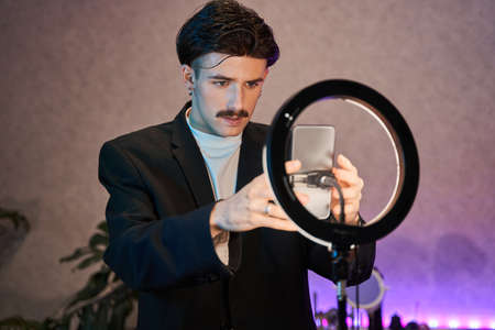 Caucasian man with mustache wearing stylish suit standing in front of the lamp