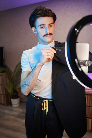 Metrosexual man showing to the camera his suit with serious face while recording his blo