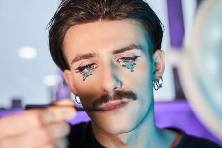 Man looking at the brush for make up and preparing creating new look at his faceの写真素材