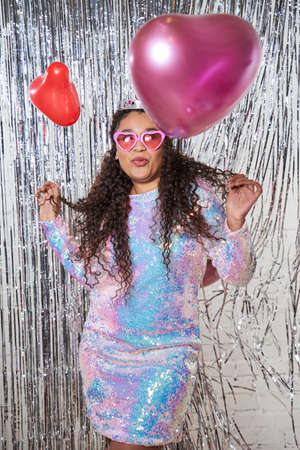 Curly hairstyle person holding balloons and looking up isolated on shiny decorated silver curtain