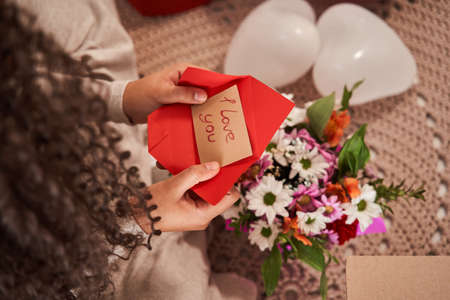 Curly woman holding greeting card with I love you signs at her hands