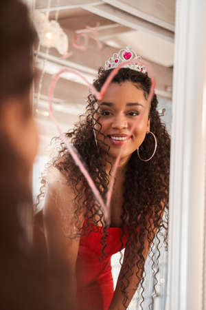 Adorable curly woman looking at the mirror at her reflection while preparing to the datingの写真素材