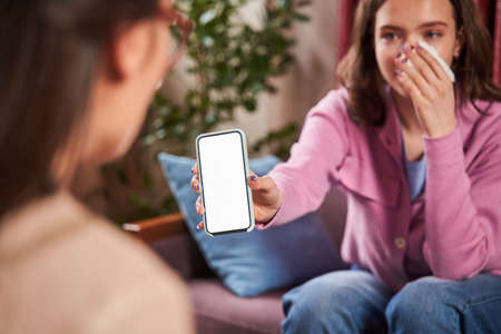 Teenager girl crying and showing smartphone to her doctor while spending time at the session