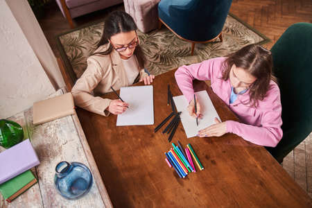 Teen patient sitting at the table and drawing at the paper in therapist session