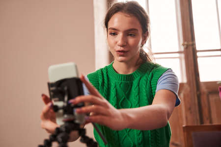 Female teenager adjusting her smartphone on tripod and preparing recording her video blog
