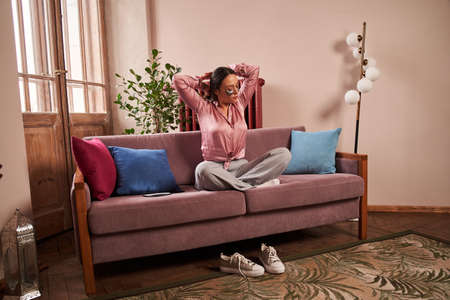 Woman sitting at the sofa and relaxing at the lotus pose while doing beauty routine at homeの写真素材