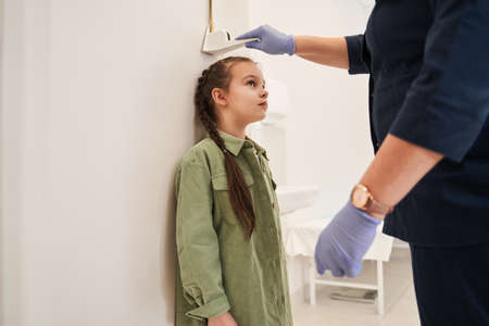 Female doctor measuring height of little girl in clinic