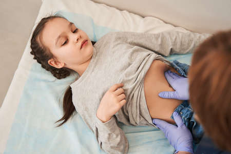 Unrecognizable doctor palpating belly of little girl lying on couch in doctors office and smilingの写真素材