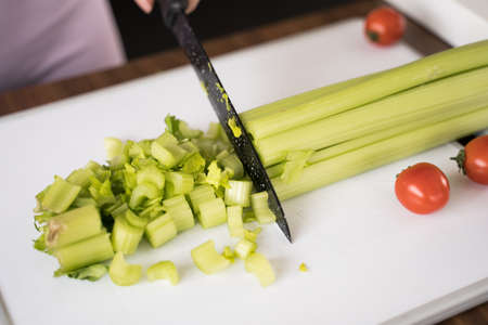 Female person chopping celery at the board at home while cooking healthy saladの写真素材