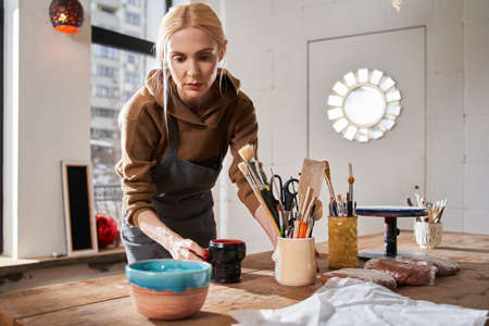 Woman preparing her workplace while putting different things at the table with concentrated face