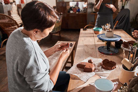 Woman sitting at the table and preparing making something from clay with special stickの写真素材