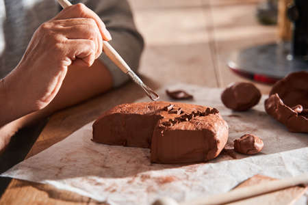 Mature woman holding special sculpting stack and using it at the piece of clayの写真素材