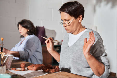 Mature woman holding special sculpting stack and using it at the piece of clayの写真素材