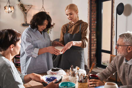 Female teacher giving plate with glaze to her mature studentの写真素材