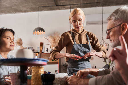 Craftswoman wearing apron explaining to her students how to make clay dishes in pottery workshopの写真素材