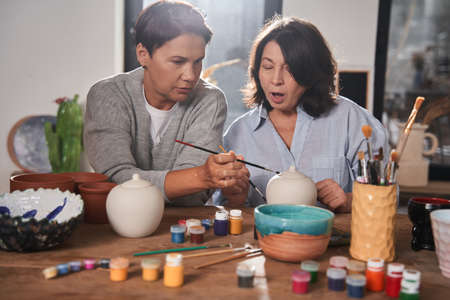 Two mature woman sitting at the table in pottery master classの写真素材