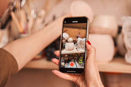 Woman artist shooting ceramic vase and cups at the smartphoneの写真素材
