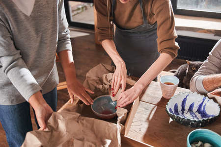 Two women putting new hand made plate at the paper and cupboard box while packingの写真素材
