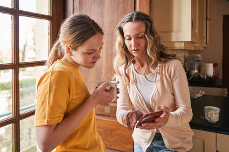 Teenage girl looking at the smartphone screen while her mother showing something to herの写真素材