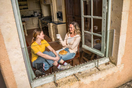Teenage daughter chatting with her happy mom while enjoying morning