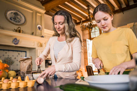 Girl preparing vegetables for the future salad while standing near motherの写真素材