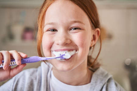 Red-haired pretty child cleaning her teeth in diligent way