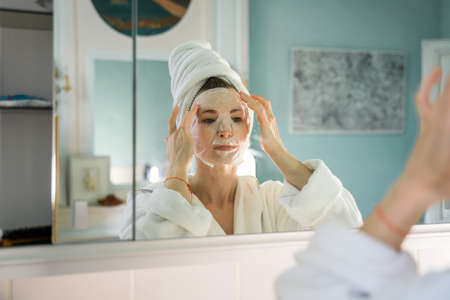 Reflection at the mirror of the adult woman applying face mask