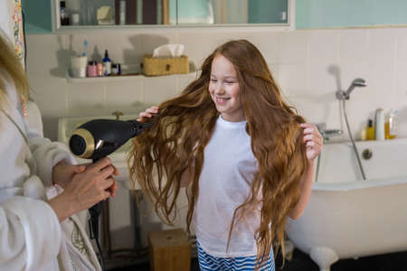 Woman wiping hair with the hair dryer to her little daughter at the bathroom