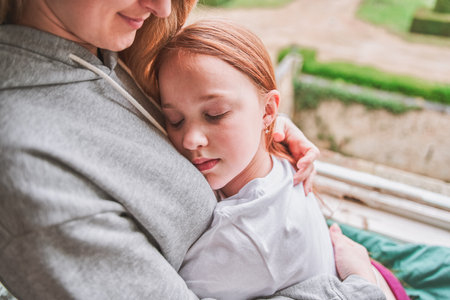 Little happy girl hugging mom, she leaning at female shoulder embracing her with both handsの写真素材