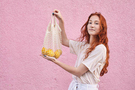Vegetarian cheerful woman holding package with orange fruitsの写真素材