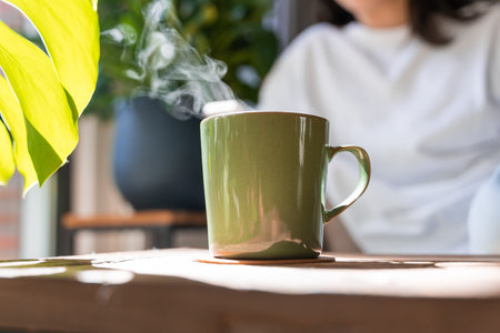 Cropped view of the green mug with tea standing at the tableの写真素材