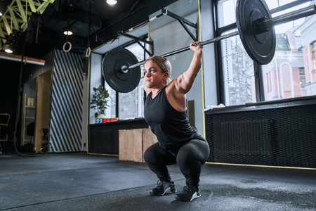 Midget woman squatting in a sports hall and holding barbell