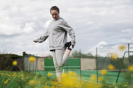 Female teenager stretching her leg at the summer field while