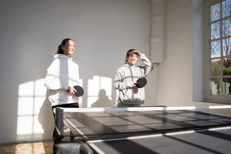 Mother and daughter playing tennis table at home during sunny