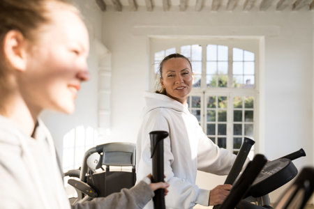 Careful mother exercising on elliptical cross trainer with