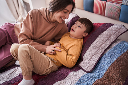 Sweet boy with Down syndrome laying at the bed while playingの写真素材
